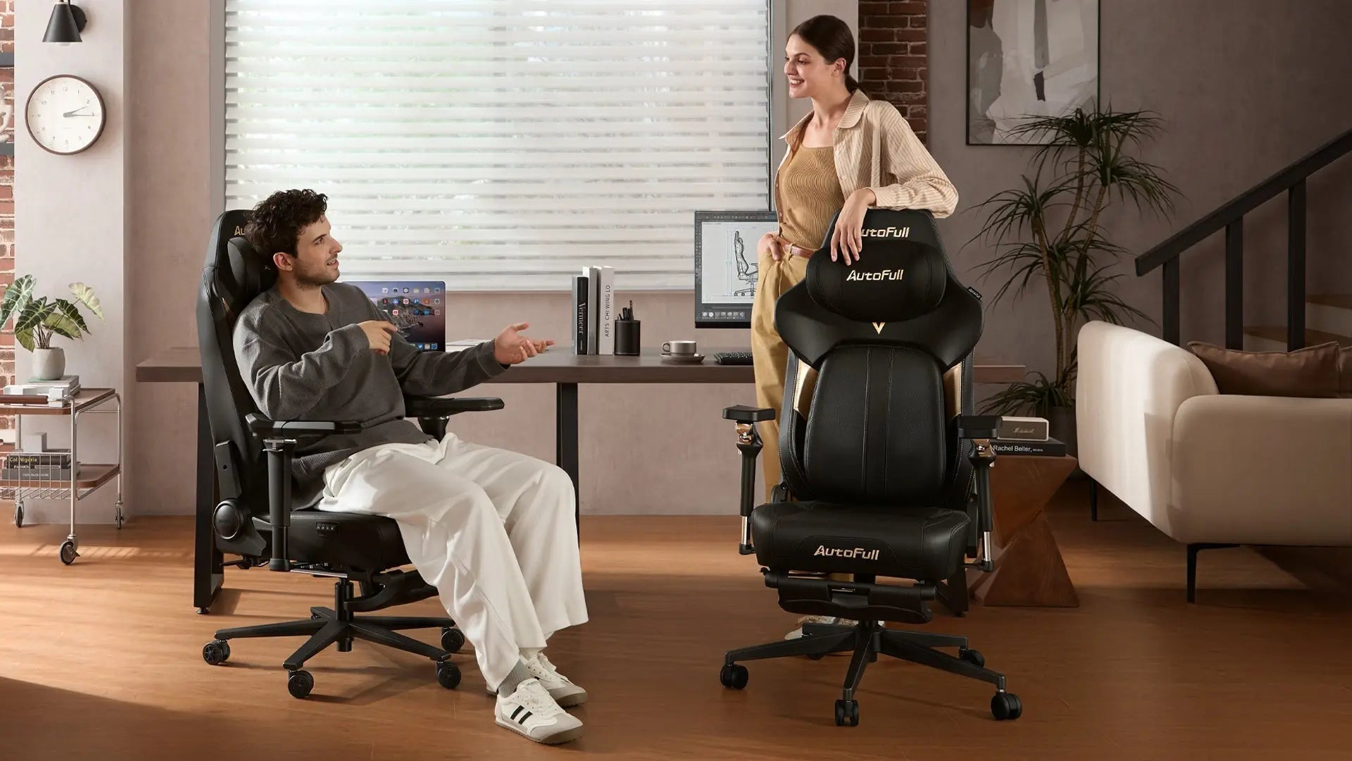 A man and woman talk in an office setting with two AutoFull ergonomic black gaming chairs.